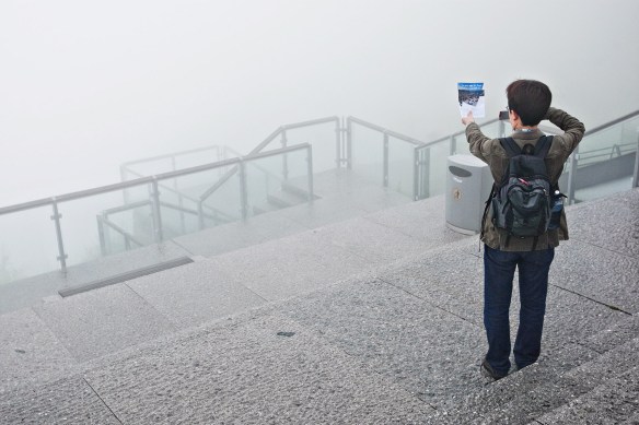 Mr. Hideyuki Uchida from Matsuyama in Japan photographs a brochure showing the view from mount Fløien the way it's supposed to be. Mr. Uchida onlys has nine days for all three of the Nordic countries, leaving him with no time to wait for the fog to clear.